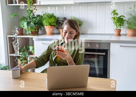 Lächelnde, zufriedene Frau, die freiberuflich arbeitet, die Pause verzögert, im Internet auf dem Handy surft. Stockfoto