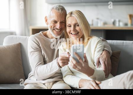 Ein fröhliches Paar genießt eine gute gemeinsame Zeit, während es auf ein Smartphone schaut Stockfoto