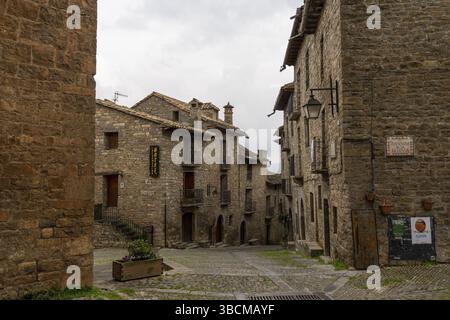 Ainsa, Spanien - 6. März 2021: Horizontale Ansicht einer engen Kopfsteinpflasterstraße mit massiven braunen Steinhäusern Stockfoto