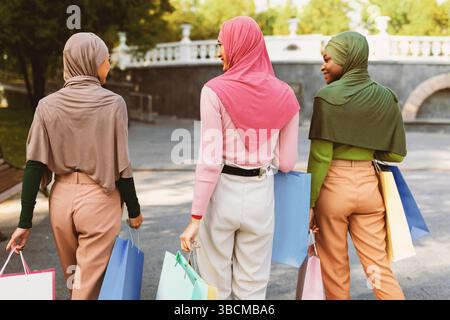 Drei Muslimische Frauen, Die Nach Dem Einkaufen Im Freien Mit Taschen Spazieren, Rückansicht Stockfoto