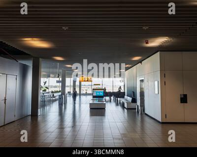 AMSTERDAM, NIEDERLANDE - 21. AUGUST 2024: Ruhiger Innenraum des Schiphol Gate E24 von Amsterdam zeigt leere geflieste Lounge, Bänke, Informationsleinwände und To Stockfoto