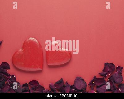 Rustikale Holzherzen mit Rosenblättern auf rotem Hintergrund mit Leerzeichen für Text Stockfoto