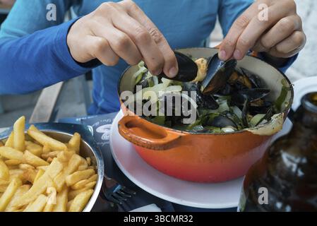 Horizontale Ansicht der Hände einer Frau, die traditionelle Muschel und Pommes Frites-Gericht isst Stockfoto