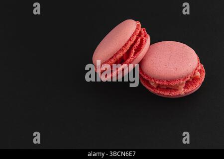 Zarte rosafarbene Macarons sitzen auf einer eleganten schwarzen Oberfläche mit einer glatten Textur. Ihre leuchtenden Farben verleihen jedem dess einen Hauch von Eleganz Stockfoto