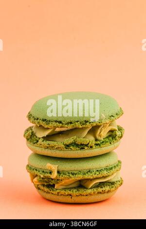 Zwei köstliche grüne Macarons sind aufeinander gestapelt und präsentieren eine cremige Füllung vor einem warmen pfirsichfarbenen Hintergrund, die ihre ansprechende Farbe unterstreicht Stockfoto