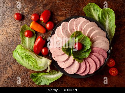 Verschiedene gekochte Würstchen mit Gemüse und Gemüse auf braunem Vintage-Hintergrund. Stockfoto