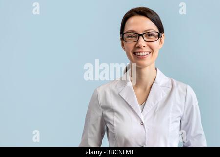 Ärztin im Laborkittel lächelt vor blauem Hintergrund Stockfoto