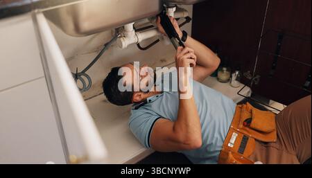 Mann, Klempner und Reparatur in der Küche, Rohr und Spülbecken mit Suche nach Lecks, Problemlösung und Bewertung zu Hause. Oben, Handwerker und Werkzeuge für die Arbeit Stockfoto