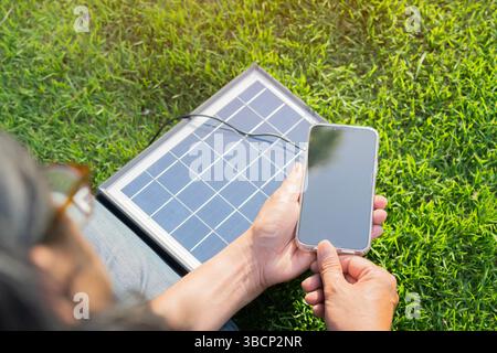 Nahaufnahme einer Person, die ein Smartphone mit einem tragbaren Solarpanel auflädt. Rückansicht, selektiver Fokus. Stockfoto
