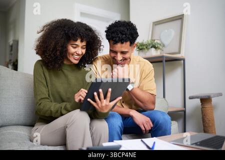 Ein lächelndes Paar, das einen Moment gemeinsam erlebt, während es ein Tablet im modernen Wohnzimmer sieht Stockfoto