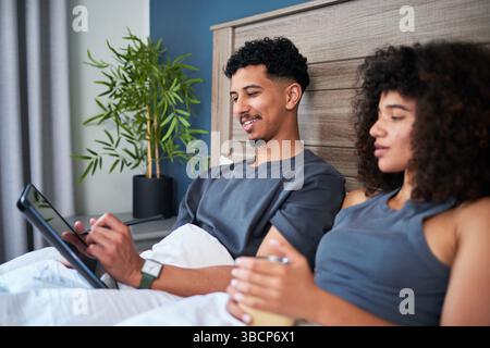 Entspannen Sie sich im Bett, während Sie eine gute Zeit miteinander verbringen und Geräte genießen Stockfoto
