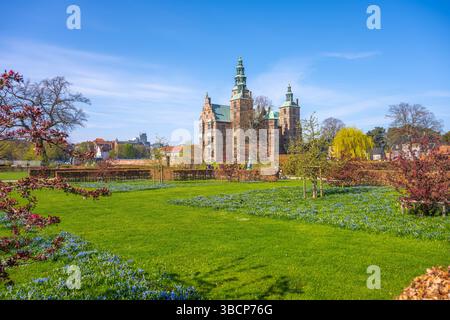 Schloss Rosenborg steht majestätisch in Kopenhagen, Dänemark, umgeben von lebendigen Gärten. Besucher schlendern durch grüne Rasenflächen und genießen die Frühlingsblüten und die ruhige Atmosphäre. Stockfoto