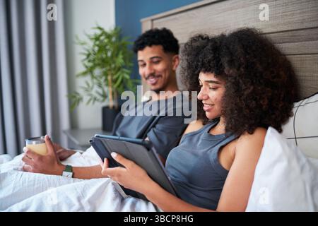 Entspanntes Paar, das an einem komfortablen Morgen gemeinsam die Freizeit in gemütlicher Schlafzimmerumgebung genießt Stockfoto