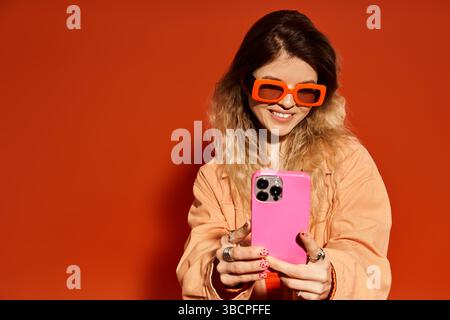 Eine junge Frau im trendigen Outfit lächelt beim Selfie in leuchtendem Orange. Stockfoto