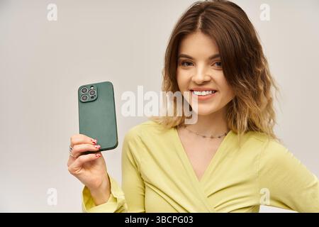 Eine schöne junge Frau lächelt selbstbewusst in einem modischen Outfit vor grauem Hintergrund. Stockfoto
