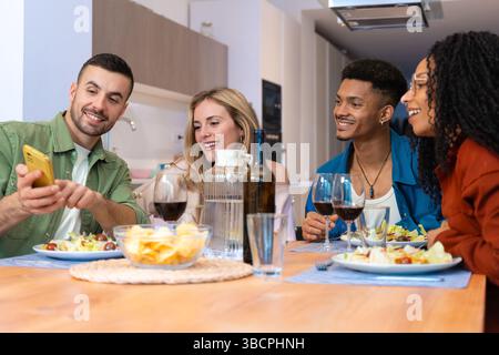 Fröhliche multiethnische Freunde genießen Snacks und Getränke in moderner, heller Küche Stockfoto