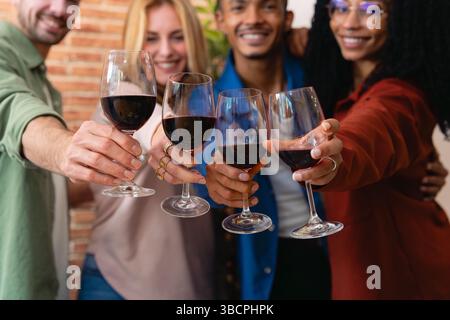 Multiethnische Gruppe glücklicher Freunde, die bei einem fröhlichen Treffen mit Rotwein tosten Stockfoto