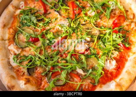 Nahaufnahme von frischer Gemüsepizza mit Rucola in Karton auf Holztisch, Blick von oben, Sonnenlicht Stockfoto