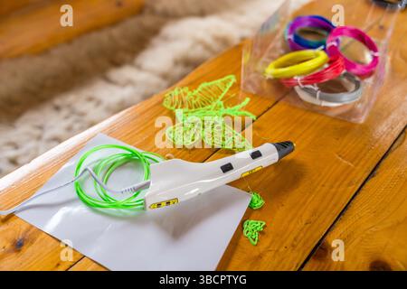 3D-Druckstift und bunte Filamente auf Holztisch mit grüner Schmetterlingsform, selektiver Fokus Stockfoto
