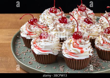 Schokoladen-Cupcakes mit Schlagsahne Maraschino-Kirschen und Schokoladenspänen auf grüner Platte. Stockfoto