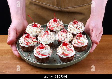 Schokoladen-Cupcakes mit Schlagsahne Maraschino-Kirschen und Schokoladenspänen auf grüner Platte. Stockfoto