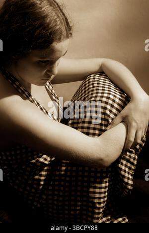 Depressive junge Frau sitzt mit Armen um die Knie und blickt in emotionaler Not nach unten. USA. Stockfoto