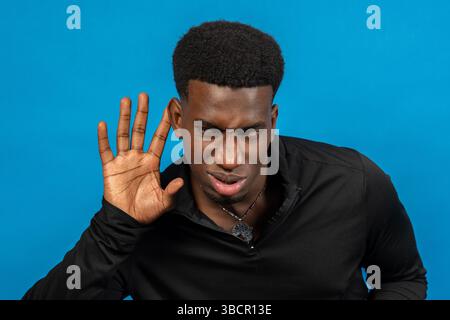 Neugieriger Mann, der aufmerksam zuhört, Hand an Ohr hält, versucht, Gespräche zu hören, lauscht, hört Klatsch zu, Studio auf blauem Hintergrund gedreht Stockfoto