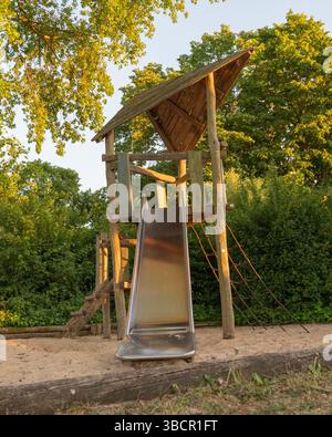 Ein wunderschöner Holzspielplatz mit einer hellen Rutsche und mehreren üppigen Bäumen im Hintergrund, die eine schöne Atmosphäre im Freien für Chi schaffen Stockfoto