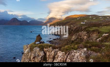 Ein Fotograf fängt die dramatische Cuillin-Gebirgskette von den Klippen nahe Elgol Village auf der Isle of Skye in Schottland während der goldenen Stunde ein Stockfoto