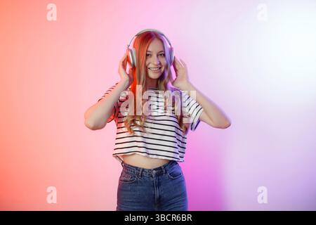 Die junge Frau genießt Musik mit Kopfhörern in einem farbenfrohen Studio-Setting an einem hellen Nachmittag Stockfoto