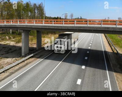 Ein großer Lkw fährt unter einer Betonüberführung auf einer ruhigen, von Bäumen umgebenen Autobahn. Stockfoto