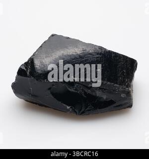 Ein roher, dunkler, glänzender Obsidian mit einer rauen, gebrochenen Oberfläche mit feinen Streifen, reflektierendem Glanz und schwarzer Farbe auf einem Stockfoto