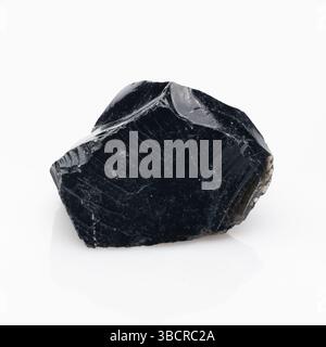 Ein markantes, rohes Stück natürliches schwarzes Obsidiangestein mit einer glänzenden, glasartigen Oberfläche, scharfen Kanten und einer gebrochenen Textur, die dunkle Farbtöne reflektieren Stockfoto