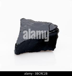 Ein markantes Stück rohen, natürlichen Obsidiangesteins mit einer glänzend schwarzen Oberfläche und scharfen, gebrochenen Kanten, präsentiert vor einem klaren, reflektierenden weißen bac Stockfoto