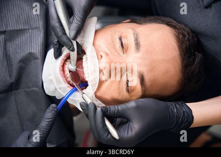 Nahaufnahme des Zahnarztes beim Bohren von Zahn an männlichen Klienten mit Mundöffner Stockfoto