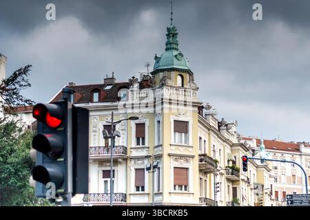 Rote Ampel mit Stoppschild mit eleganter europäischer Architektur im Hintergrund an einem bewölkten Tag Stockfoto