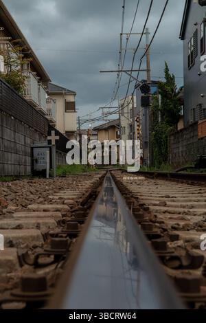 Nahaufnahme einer nassen Straßenbahnschiene und Holzschwellen auf Kamakuras Enoden-Linie mit Betonung von Textur und Detail Stockfoto