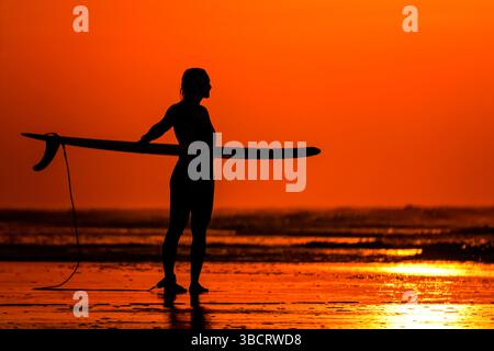 Folly Beach, Usa. Mai 2025. Eine Surferin sieht den Sonnenaufgang, als sie am 21. Mai 2025 in Folly Beach, South Carolina, zum Surf am Strand, bekannt als The Edge of America, spaziert. Quelle: Richard Ellis/Richard Ellis/Alamy Live News Stockfoto
