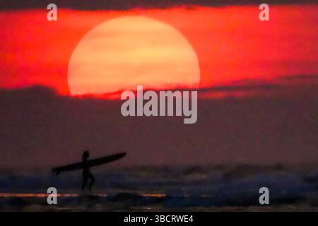 Folly Beach, Usa. Mai 2025. Eine Surferin sieht den Sonnenaufgang, als sie am 21. Mai 2025 in Folly Beach, South Carolina, zum Surf am Strand, bekannt als The Edge of America, spaziert. Quelle: Richard Ellis/Richard Ellis/Alamy Live News Stockfoto