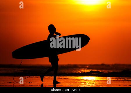 Folly Beach, Usa. Mai 2025. Ein Surfer ist vom Sonnenaufgang geprägt, als er am 21. Mai 2025 in Folly Beach, South Carolina, zum Surf am Strand, bekannt als The Edge of America, spaziert. Quelle: Richard Ellis/Richard Ellis/Alamy Live News Stockfoto