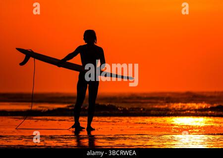 Folly Beach, Usa. Mai 2025. Eine Surferin sieht den Sonnenaufgang, als sie am 21. Mai 2025 in Folly Beach, South Carolina, zum Surf am Strand, bekannt als The Edge of America, spaziert. Quelle: Richard Ellis/Richard Ellis/Alamy Live News Stockfoto