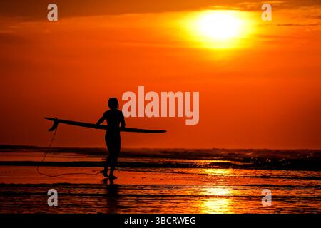 Folly Beach, Usa. Mai 2025. Eine Surferin sieht den Sonnenaufgang, als sie am 21. Mai 2025 in Folly Beach, South Carolina, zum Surf am Strand, bekannt als The Edge of America, spaziert. Quelle: Richard Ellis/Richard Ellis/Alamy Live News Stockfoto