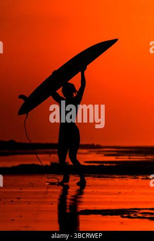 Folly Beach, Usa. Mai 2025. Eine Surferin sieht den Sonnenaufgang, als sie am 21. Mai 2025 in Folly Beach, South Carolina, zum Surf am Strand, bekannt als The Edge of America, spaziert. Quelle: Richard Ellis/Richard Ellis/Alamy Live News Stockfoto