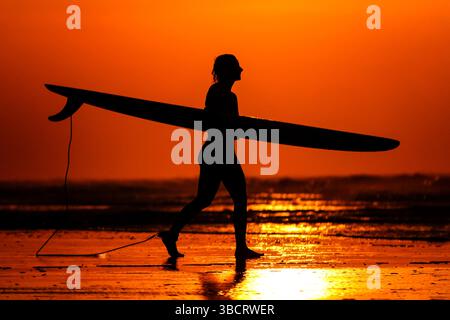 Folly Beach, Usa. Mai 2025. Eine Surferin sieht den Sonnenaufgang, als sie am 21. Mai 2025 in Folly Beach, South Carolina, zum Surf am Strand, bekannt als The Edge of America, spaziert. Quelle: Richard Ellis/Richard Ellis/Alamy Live News Stockfoto