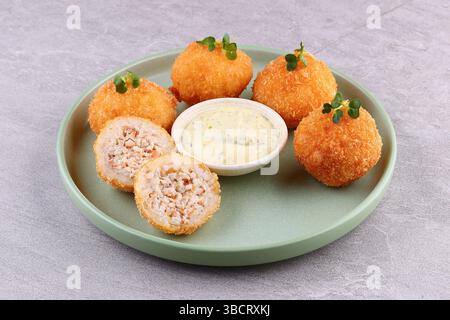 Knusprige Hühnchen-Reis-Kroketten mit cremigem Kräuter-Mayo-Dip auf grünem Teller, Blick von oben, Kopierraum. Stockfoto