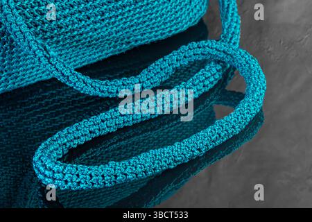 Grüne Damenhandtasche, handgestrickt, mit Brosche und langem Griff. Details und Elemente. Auf grauem Hintergrund. Stockfoto