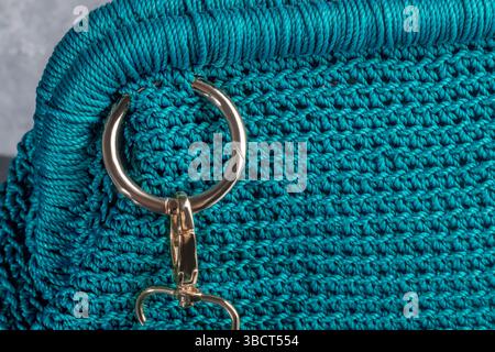 Grüne Damenhandtasche, handgestrickt, mit Brosche und langem Griff. Details und Elemente. Auf grauem Hintergrund. Stockfoto