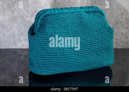 Grüne Damenhandtasche, handgestrickt, mit Brosche und langem Griff. Details und Elemente. Auf grauem Hintergrund. Stockfoto