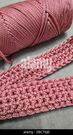 Stricken von Elementen einer rosafarbenen Damentasche, Handstricken mit langem Griff. Schritt-für-Schritt-Anweisungen. Auf grauem Hintergrund. Stockfoto