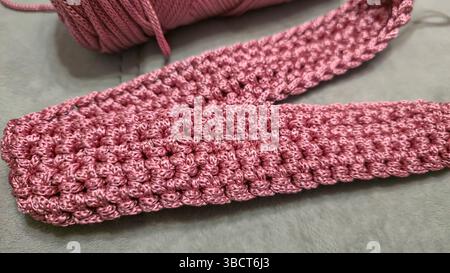 Stricken von Elementen einer rosafarbenen Damentasche, Handstricken mit langem Griff. Schritt-für-Schritt-Anweisungen. Auf grauem Hintergrund. Stockfoto